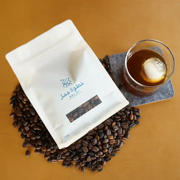 Posa piatta della busta di caffè su chicchi di caffè tostati accanto al caffè freddo per la presentazione del prodotto