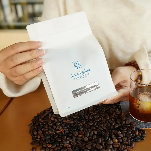 Cliente che tiene in mano una busta di caffè bianca con una scatola di carta stampata in un contesto lifestyle